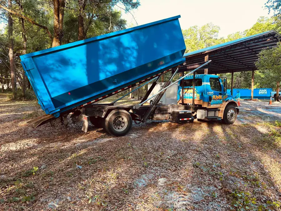 A branded Junk Sharks truck delivering a roll-off dumpster