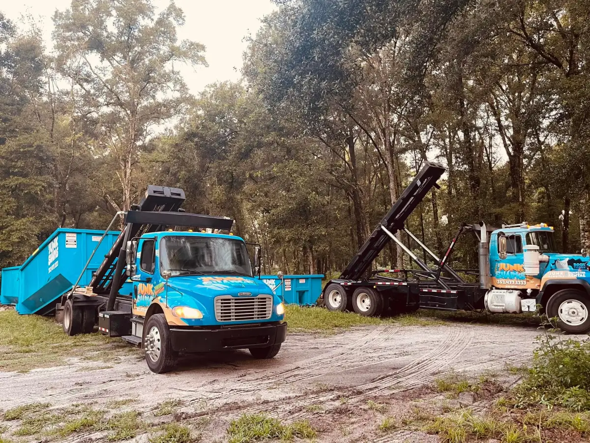 Two Junk Sharks roll-off trucks with blue dumpsters at the company yard in Ocala, Florida
