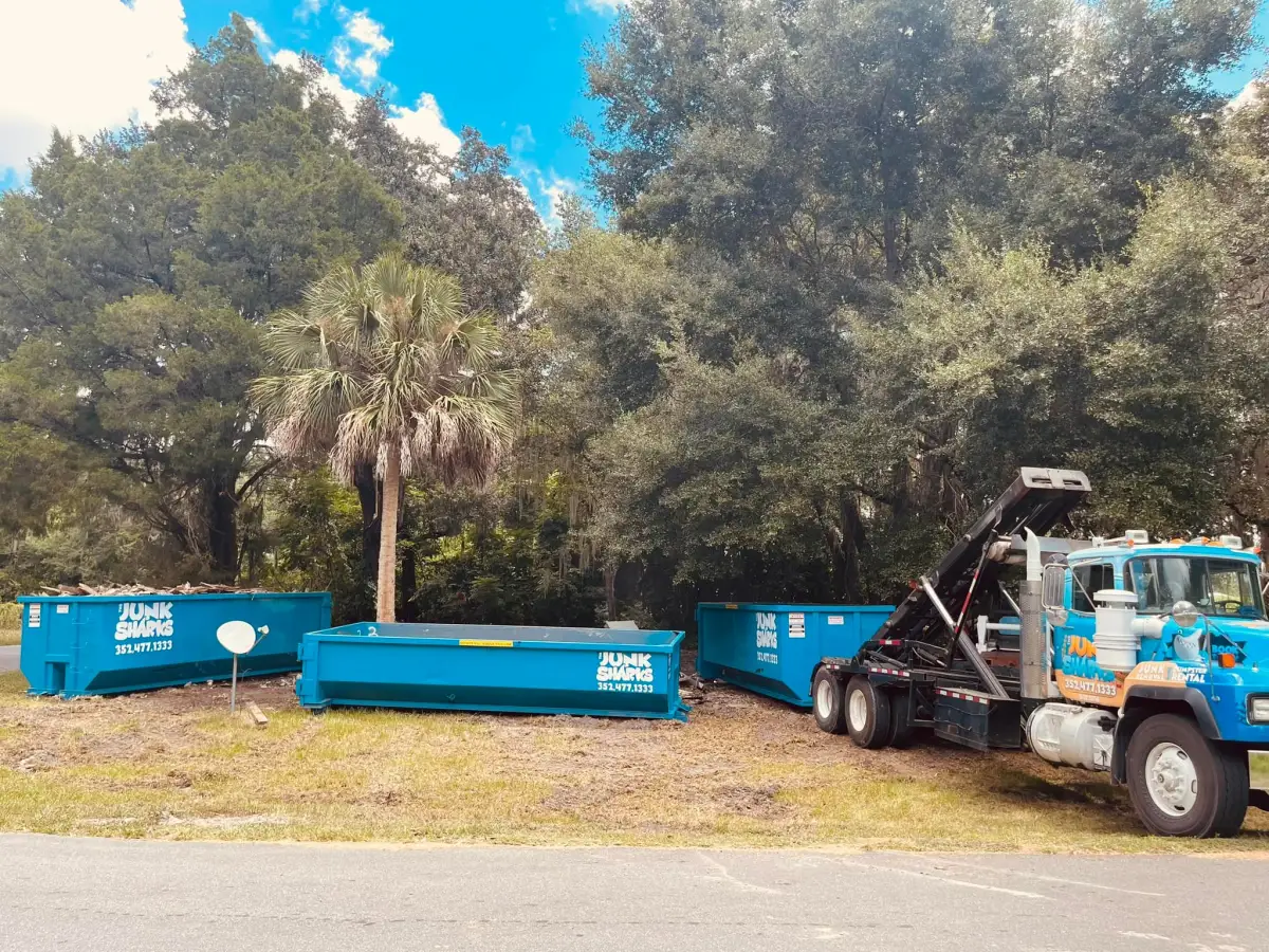 Three Junk Sharks roll-off dumpsters staged at a wooded Ocala job site with a roll-off truck